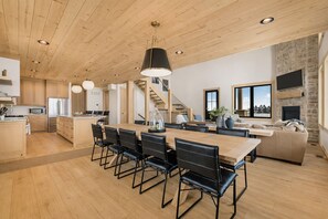A spacious kitchen with wooden cabinets, a dining area with black chairs, and a living area with a sofa and a fireplace. - New 2026 CABIN - Yellowstone 30 Min - Spa - Pickleball - Boatdock - Helipad (Island Park)