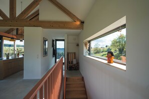 Ein modernes Interieur mit einer Holztreppe, Blick durch ein großes Fenster und einem kleinen Tisch mit einem dekorativen Gegenstand.