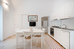 Uma cozinha moderna com armários brancos, uma mesa de jantar com cadeiras, uma televisão e uma ilha de cozinha.