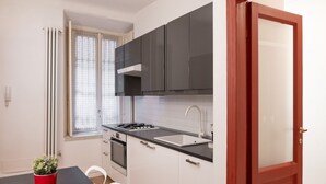 A compact kitchen with dark cabinets, a white countertop, and a red door. - Characteristic two-room apartment Colonne di San Lorenzo - Mirable PM (Milano)
