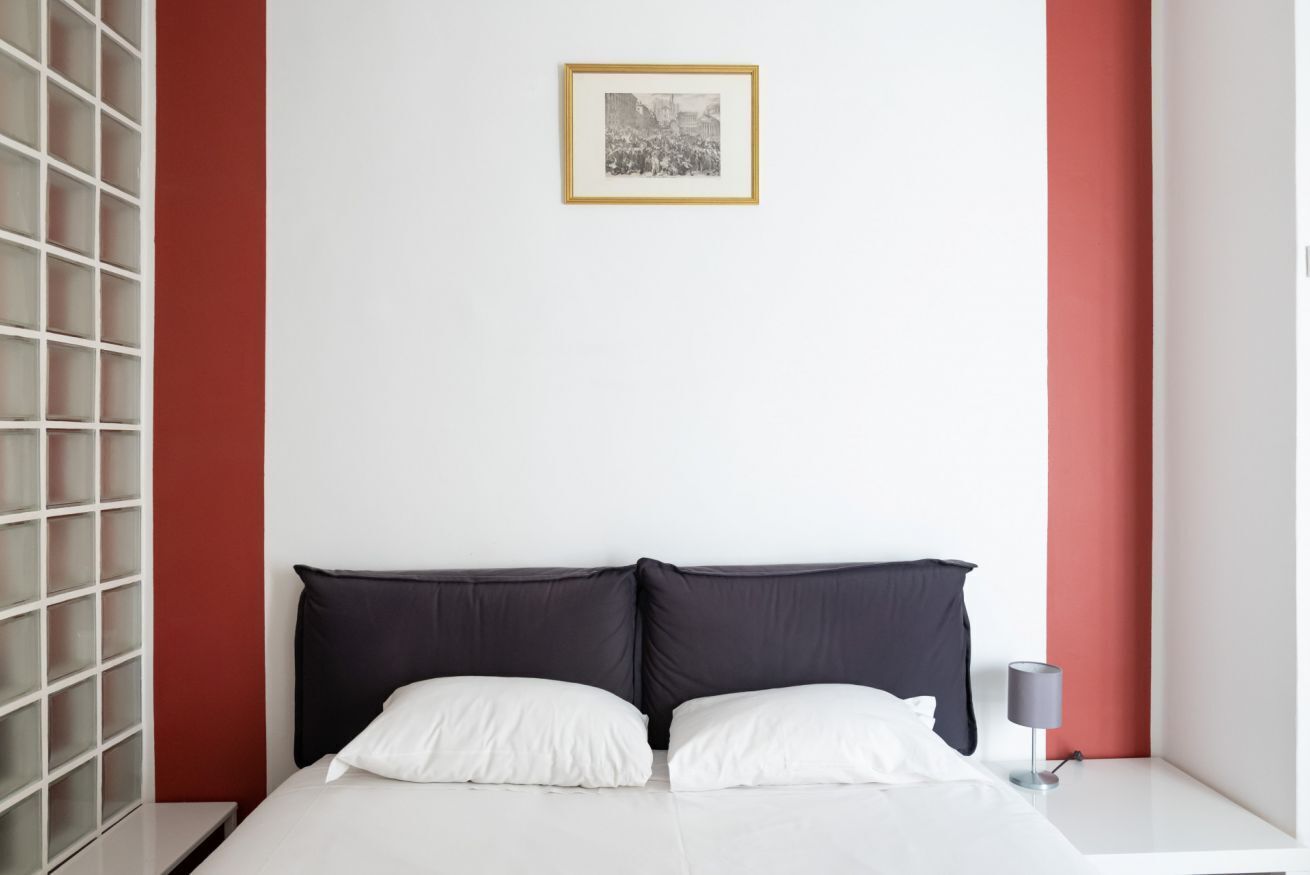 Quarto de hotel moderno com cama, mesa de cabeceira, abajur e um quadro na parede.