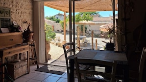 A room with a wooden table and chairs, a stone wall, and a view of the outside.