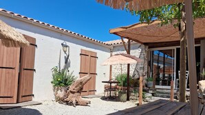A courtyard with a wooden table, a thatched umbrella, and a stone wall.