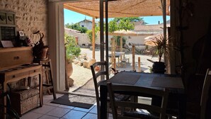 A room with a wooden table and chairs, a stone wall, and a view of the outside.