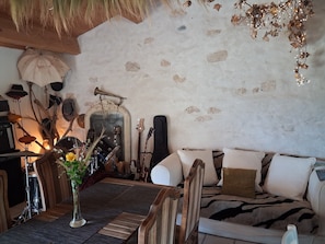 Um quarto com parede de pedra rústica, uma mesa de jantar de madeira com cadeiras, um sofá com almofadas estampadas e instrumentos musicais.