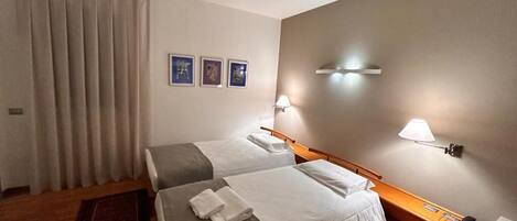 Ein Hotelzimmer mit zwei Betten, einem Holzkopfende, einem Nachttisch mit Lampe sowie einer Wandleuchte.