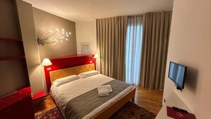 A hotel room with a large bed, a TV on the wall, a red headboard, and a window with curtains. - HOTEL CENTRALE RESANA (Resana)
