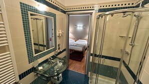 A bathroom with a glass shower enclosure, a sink with a mirror, and a door leading to a bedroom. - HOTEL CENTRALE RESANA (Resana)