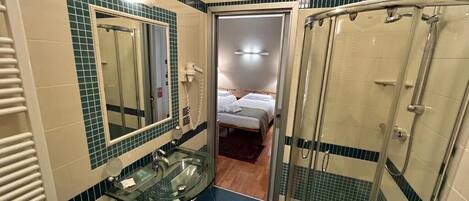 A bathroom with a glass shower enclosure, a sink with a mirror, and a door leading to a bedroom.