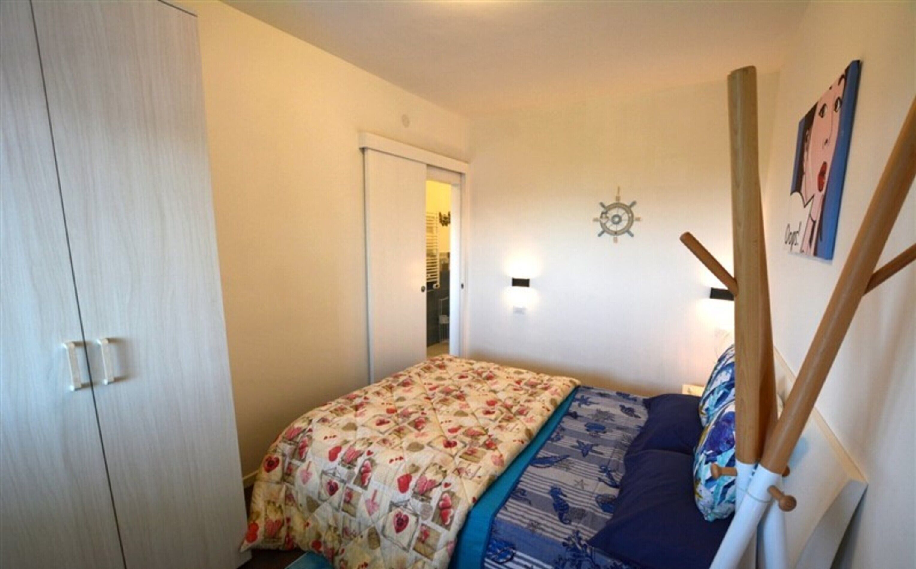 Un dormitorio con cama, armario, puerta, luz empotrada y un adorno de pared.