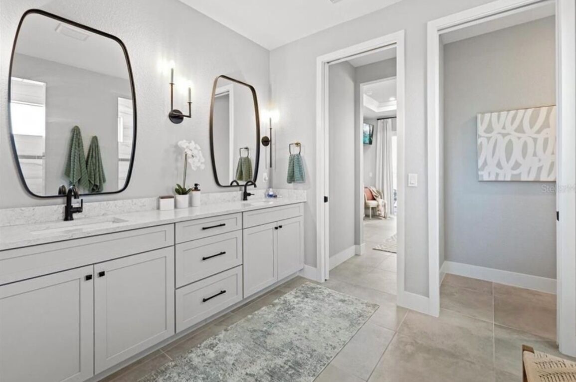 A modern bathroom with white cabinetry, a large mirror, and a light-colored rug.