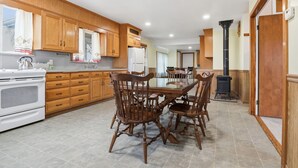 A kitchen with wooden cabinets, a stove, a dining table with chairs, and a black stove pipe. - Trackside Vacation Home - 9 min. to Sight & Sound! (Ronks)