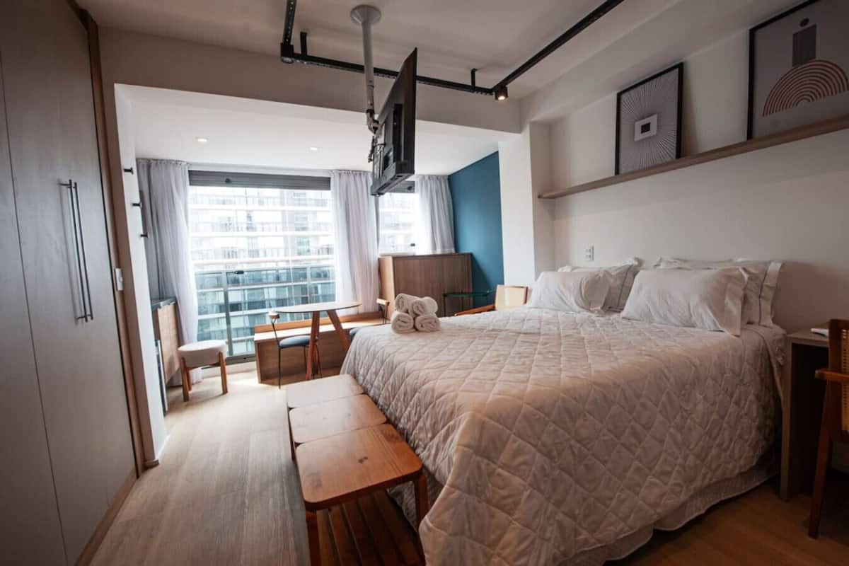Een moderne hotelkamer met een groot bed, een bureau en een stoel. Er is een televisie aan de muur bevestigd en een raam met gordijnen.