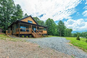 A two-story wooden cabin with a deck and a gravel driveway. - Dreamcatcher Cabin~Hot Tub, Mtn Views & Fire Pit! (Burnsville)