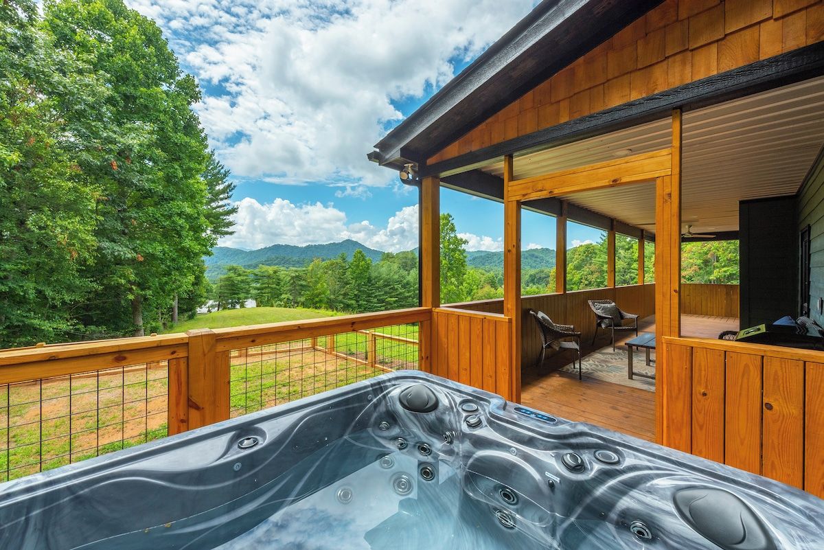 A hot tub on a wooden deck with a view of mountains and trees.