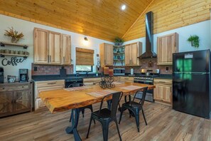 A kitchen with wooden cabinets, a large wooden dining table, and a black refrigerator. - Dreamcatcher Cabin~Hot Tub, Mtn Views & Fire Pit! (Burnsville)