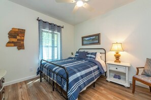 A bedroom with a bed, a nightstand, a lamp, a chair, a window with curtains, a wall clock, and a map decoration. - Dreamcatcher Cabin~Hot Tub, Mtn Views & Fire Pit! (Burnsville)