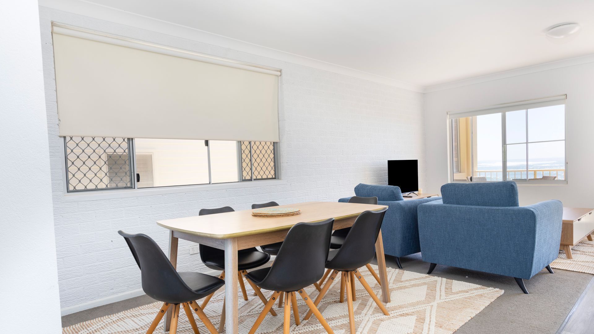 Une pièce comprenant une table à manger, des chaises, un canapé, un téléviseur et de grandes fenêtres.