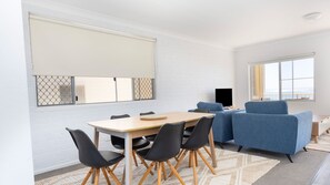 Ein Zimmer mit Esstisch, Stühlen, einer Couch, einem Fernseher und großen Fenstern.