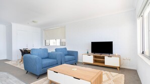 Uma sala de estar moderna com um sofá azul, uma mesa de centro de madeira, uma TV em um suporte de madeira e uma parede de tijolos brancos.