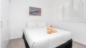 Quarto com cama, paredes brancas, um quadro emoldurado e uma janela com persianas.