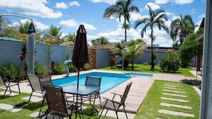 Um quintal com piscina, móveis de jardim e palmeiras.