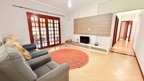 Sala de estar com sofá, televisão, tapete vermelho e porta de correr de vidro.