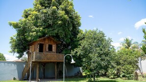 Uma casa de madeira com varanda, rodeada por vegetação exuberante e um céu azul límpido.