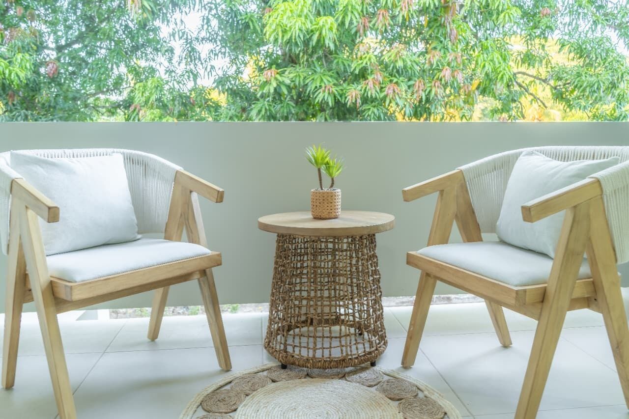 Two wooden chairs with white cushions and a woven table with a small plant.