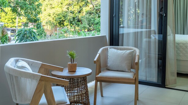 A balcony with wicker chairs, a small round table with a plant, and a woven rug.