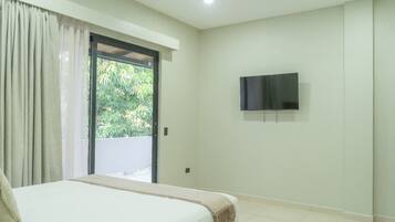 A bedroom with a bed, a TV mounted on the wall, and a sliding glass door leading to a balcony.