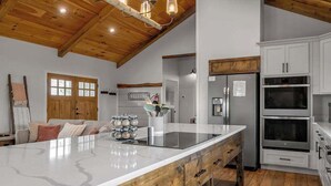 Una cocina amplia con una isla grande, techo de madera, armarios blancos y electrodomésticos de acero inoxidable.
