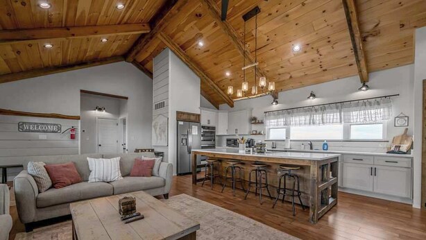 Amplia sala de estar con sofá, mesa de centro e isla de cocina con taburetes.