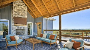 Un área de estar al aire libre con techo, chimenea de piedra, mobiliario de madera y vistas al paisaje.