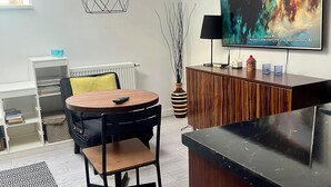 En moderne stue med et rundt træbord, sorte stole, en geometrisk lampe, et fladskærms-TV og et træskab.