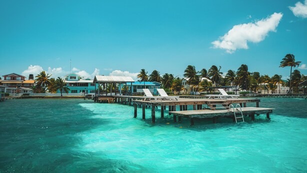 A tropical resort with a pier extending into turquoise waters, featuring overwater bungalows and palm trees. - Casa Al Mar Belize (St. George's Caye)