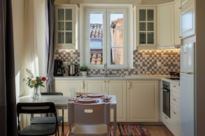 A kitchen with white cabinets, a tiled backsplash, a window with a view, a dining table set with plates and glasses, and a coffee maker. - The Lucky 12 (Kerkira)