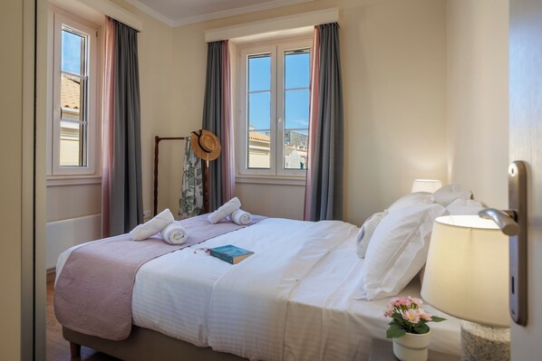 Une chambre d’hôtel avec un lit, une fenêtre, une lampe et un chapeau posé sur un présentoir.