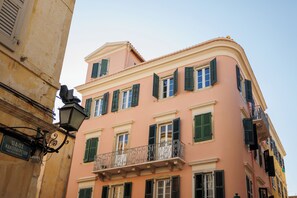 Un bâtiment rose avec des volets verts et un balcon.