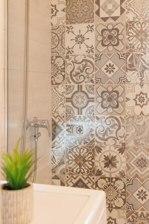 Une salle de bain avec des carreaux décorés, une douche et une plante en pot.