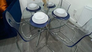 A dining area with a glass table, blue chairs, white plates, and a decorative vase with pampas grass. - Stylish 2bedroom Flat in London|free parking|Contractors (Wallington)