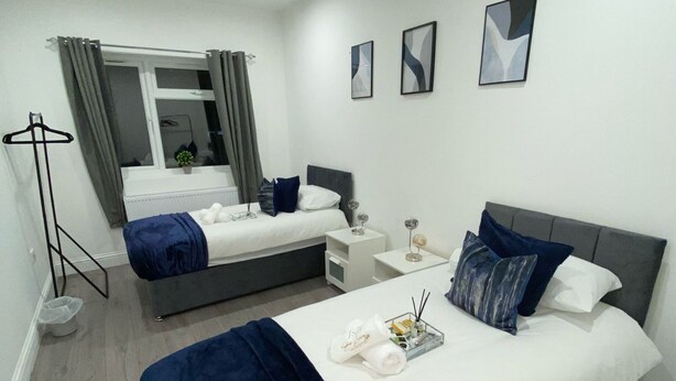A modern hotel room with two beds, a bedside table with a lamp, a small side table, and a floor lamp. - Stylish 2bedroom Flat in London|free parking|Contractors (Wallington)