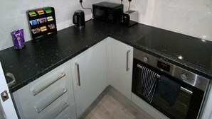 A compact kitchen with white cabinets, a black countertop, a microwave, a toaster, and a dishwasher. - Stylish 2bedroom Flat in London|free parking|Contractors (Wallington)