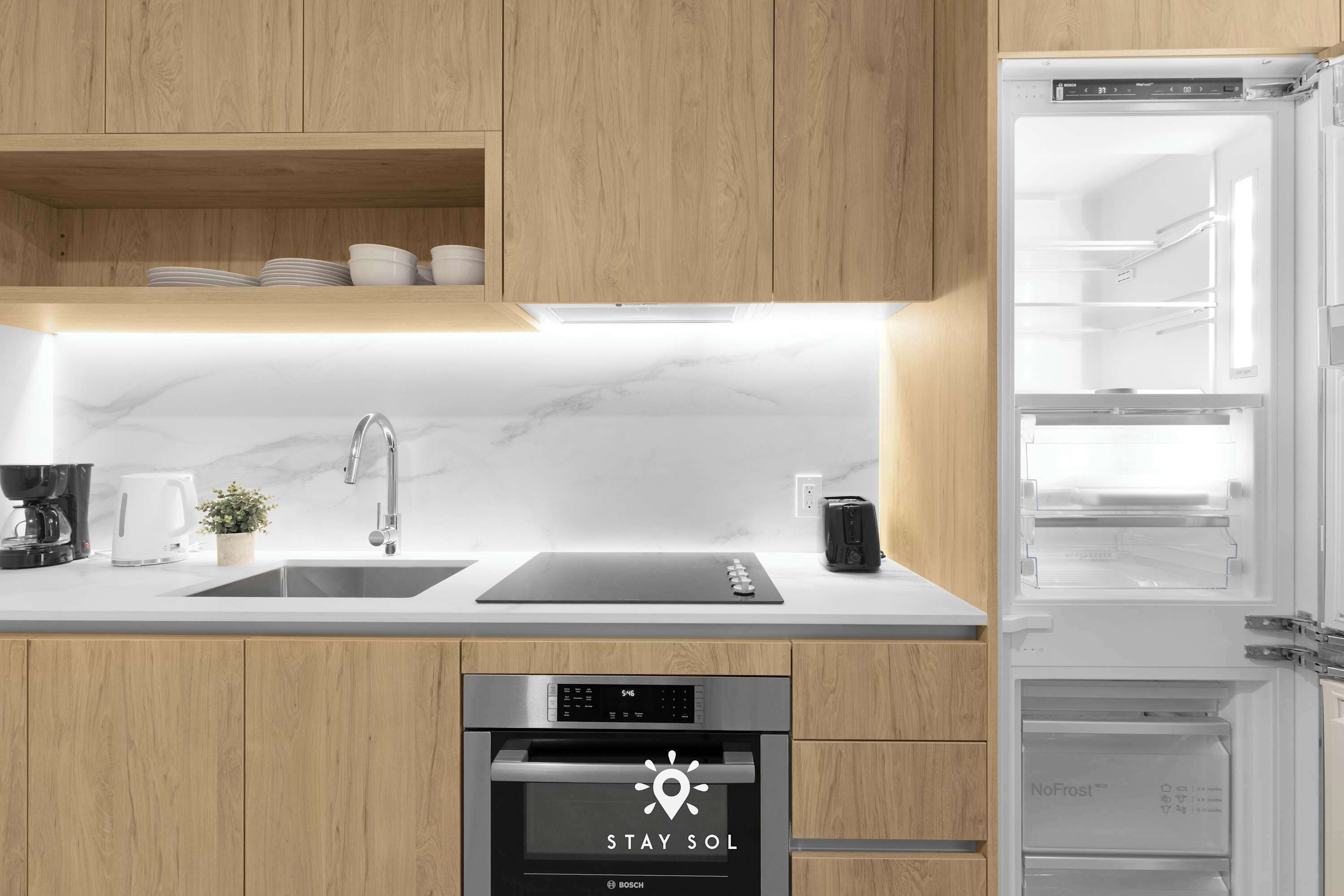 A modern kitchen with wooden cabinets, a Bosch oven, a sink, and a refrigerator.