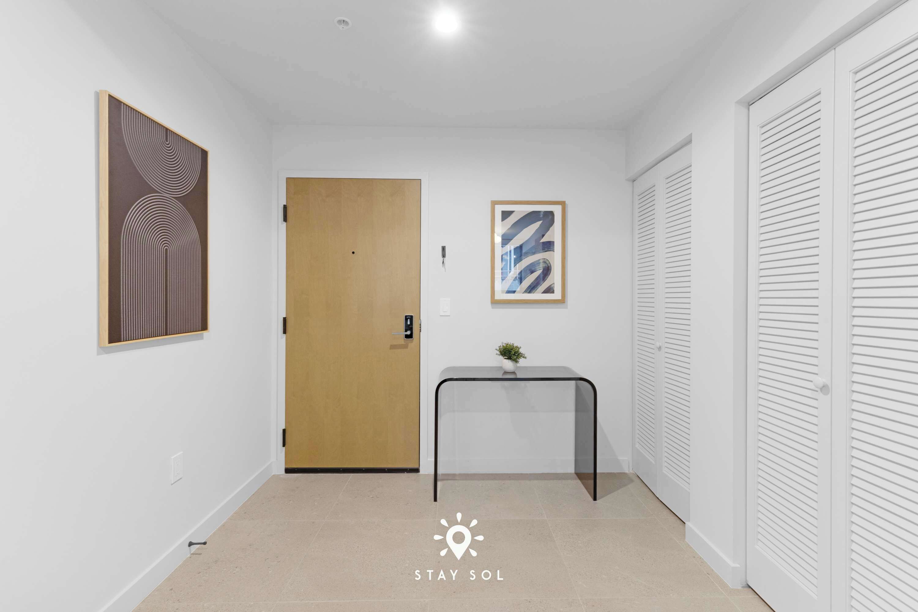 A hallway with a wooden door, a small table with a plant, and a framed abstract painting on the wall.