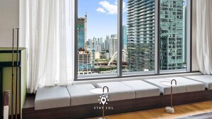 Ein modernes Hotelzimmer mit großem Fenster und Blick auf die Stadt, einer Schlafcouch und einem kleinen Tisch.