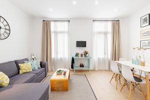 Una sala de estar moderna con sofá, mesa de centro, mesa de comedor y televisor montado en la pared.