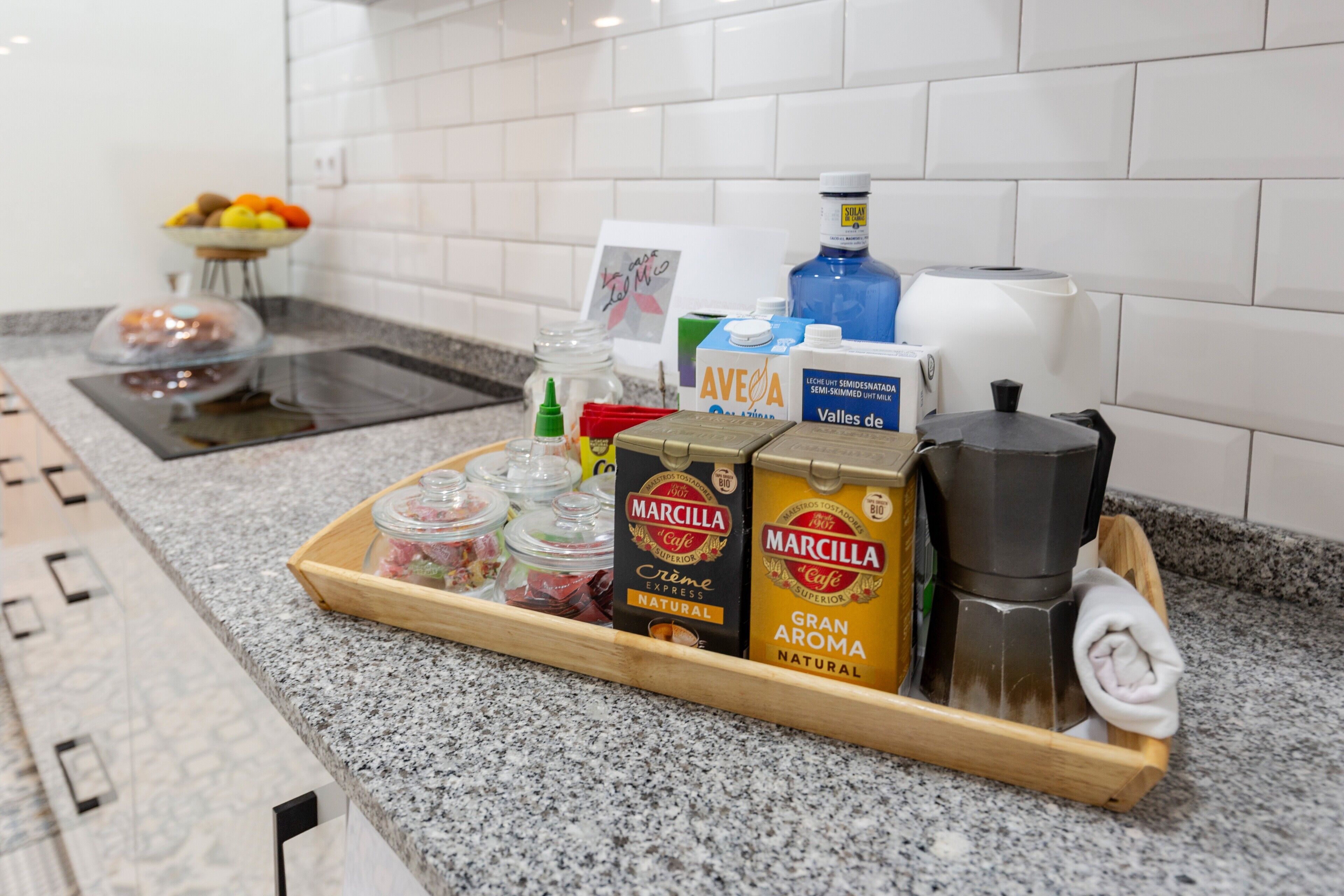 A kitchen counter with a tray containing coffee beans, a coffee grinder, a milk carton, and a bottle of water.