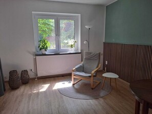 A room with a window, radiator, chair, table, and floor lamp. - Vacation apartment MoorZeit Hambergen-Ströhe (Hambergen)