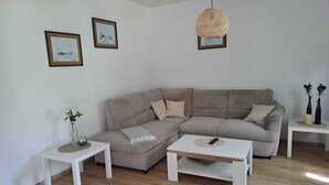 Ett vardagsrum med en beige hörnsoffa, två vita sidobord, ett vitt soffbord och en hängande lampa med flätad skärm.